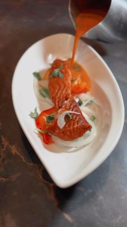 Chicken tikka masala served with sauce poured over salmon pieces, garnished with herbs and cherry tomatoes in a white dish