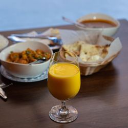 A glass of mango lassi with Indian dishes including chicken tikka masala and garlic naan bread on a wooden table.