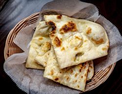 Garlic naan pieces served in a basket lined with parchment paper, showcasing light charring and a soft texture.