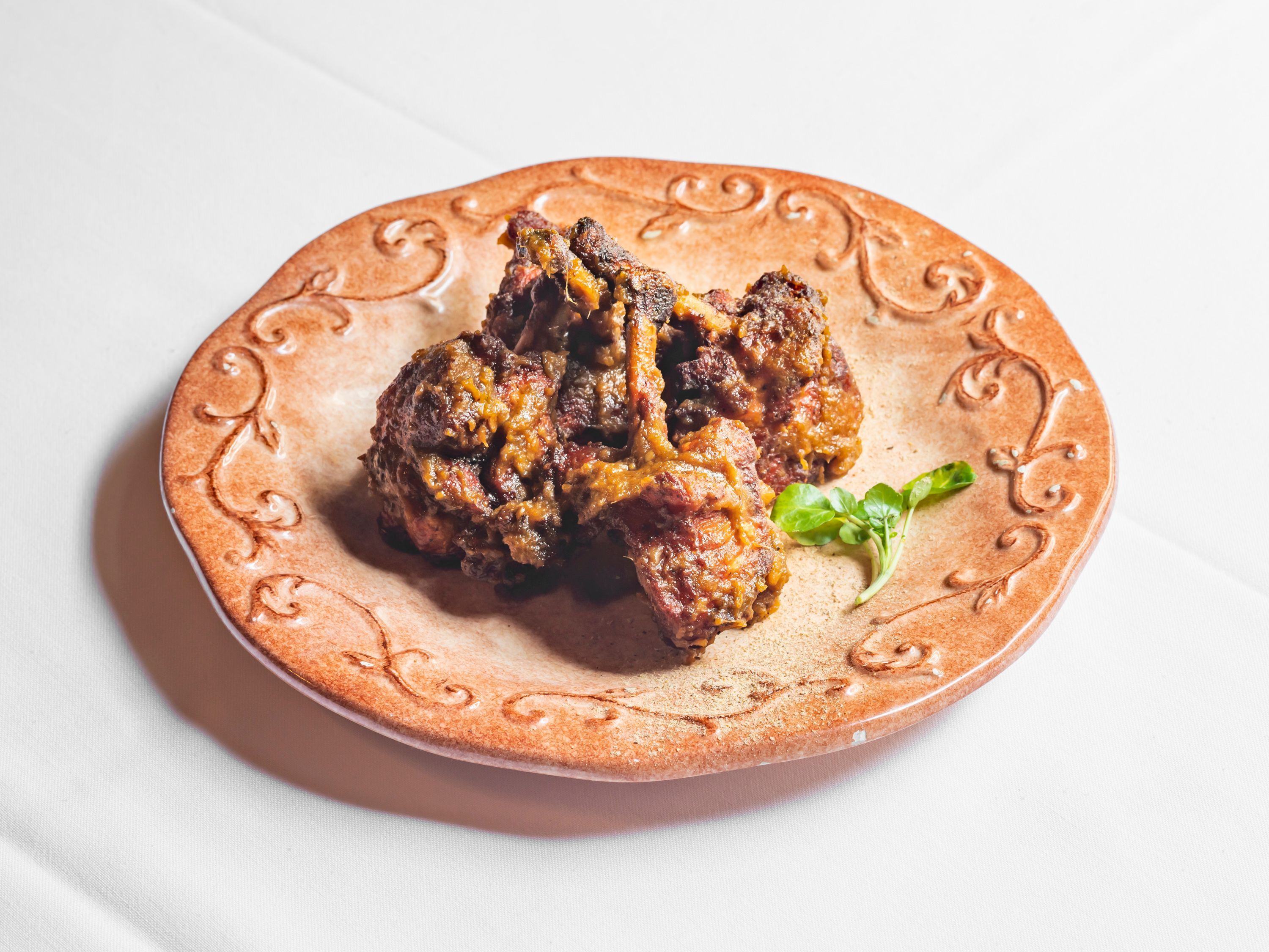 Chicken tikka masala served on a decorative brown plate with a small green garnish on the side.