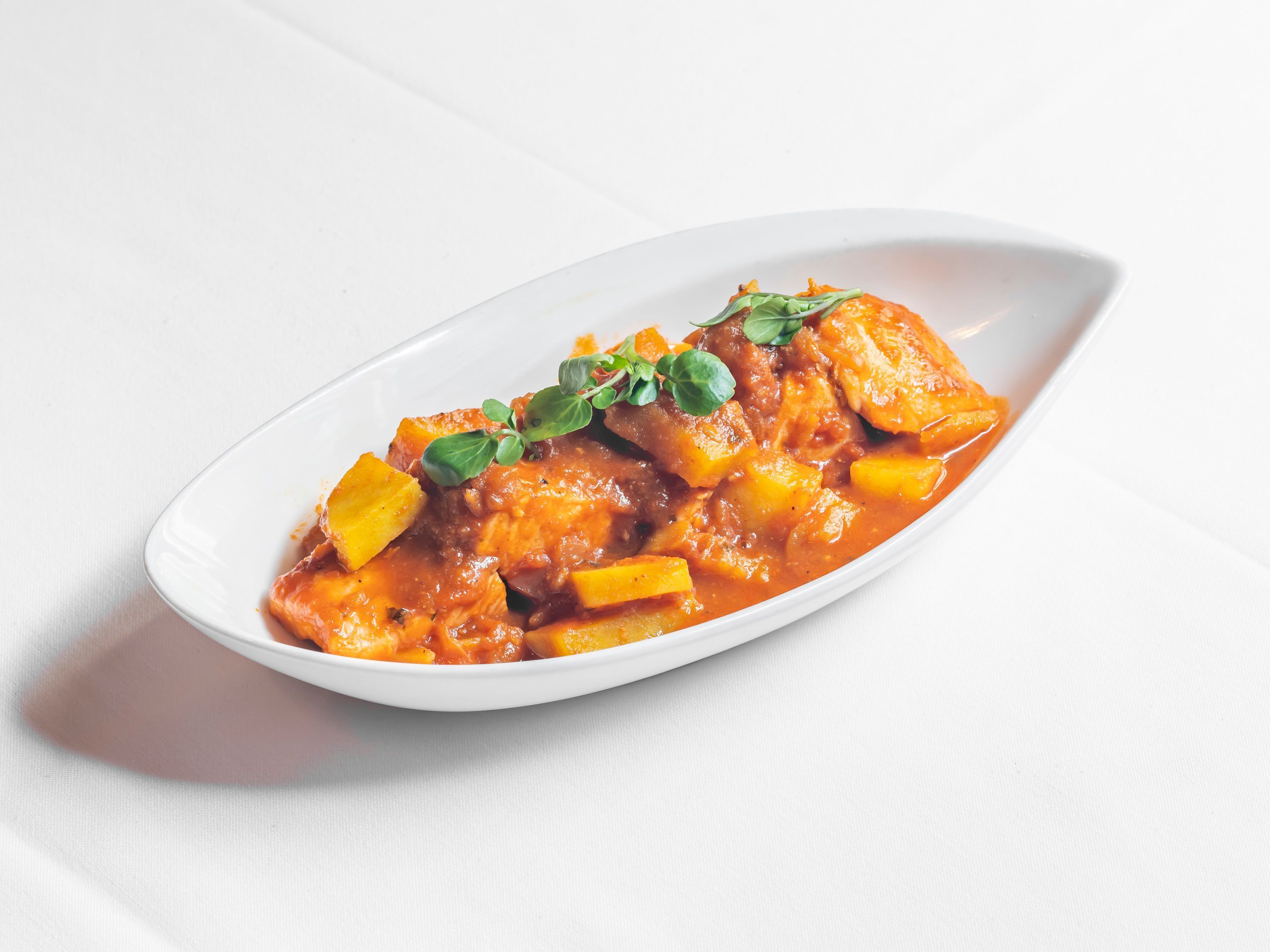Chicken tikka masala served in a white oval dish with a garnish of fresh green herbs on a white tablecloth.
