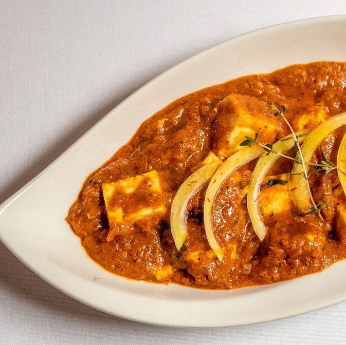 Indian cuisine dish with paneer cubes in a rich, spiced sauce garnished with onion slices and herbs on a white plate.