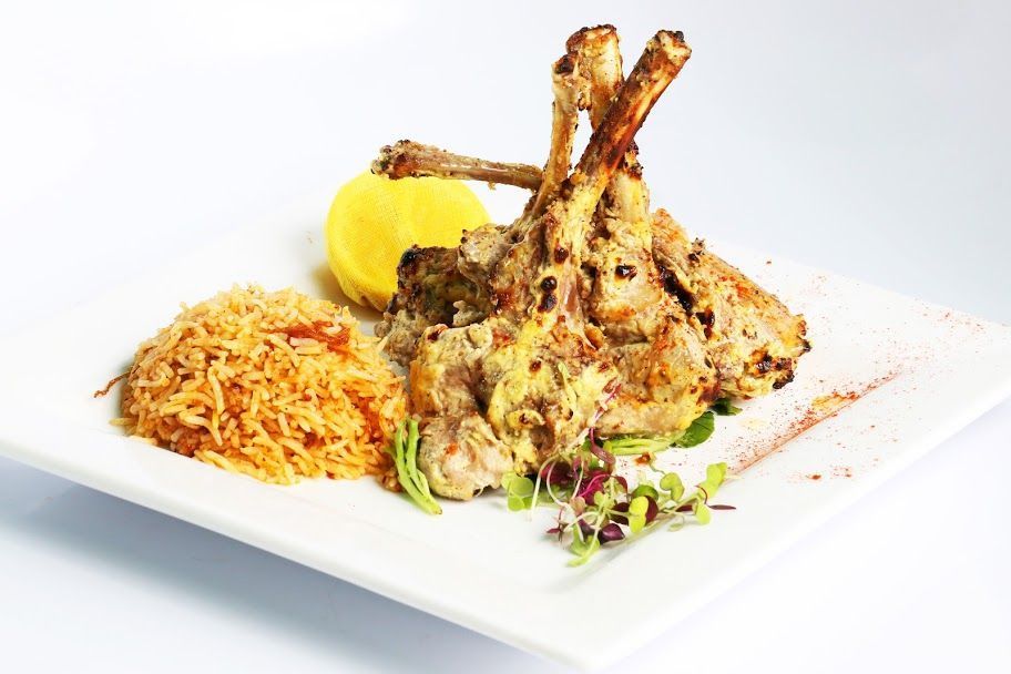 Grilled lamb chops served with seasoned rice and a lemon wedge on a white rectangular plate at Tandoor Oven.