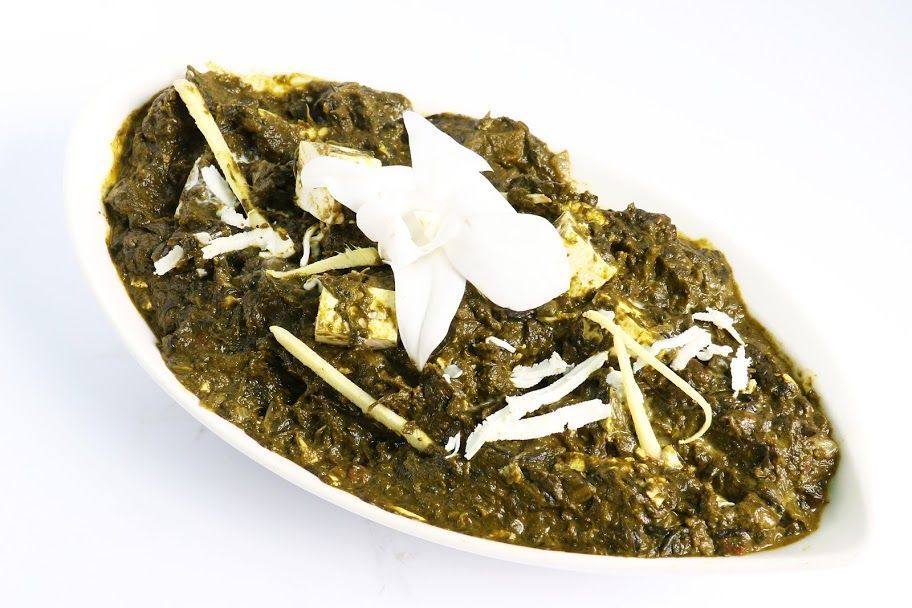 Palak paneer dish topped with ginger slices and a white edible flower, served on a white oval plate.