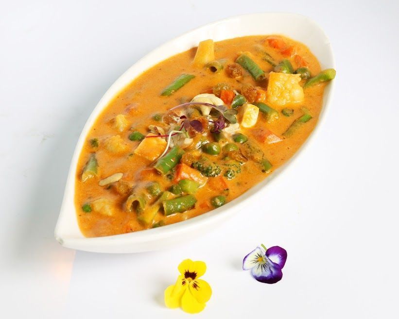 Mixed vegetable curry in a white bowl with garnish, served at Tandoor Oven Indian restaurant.